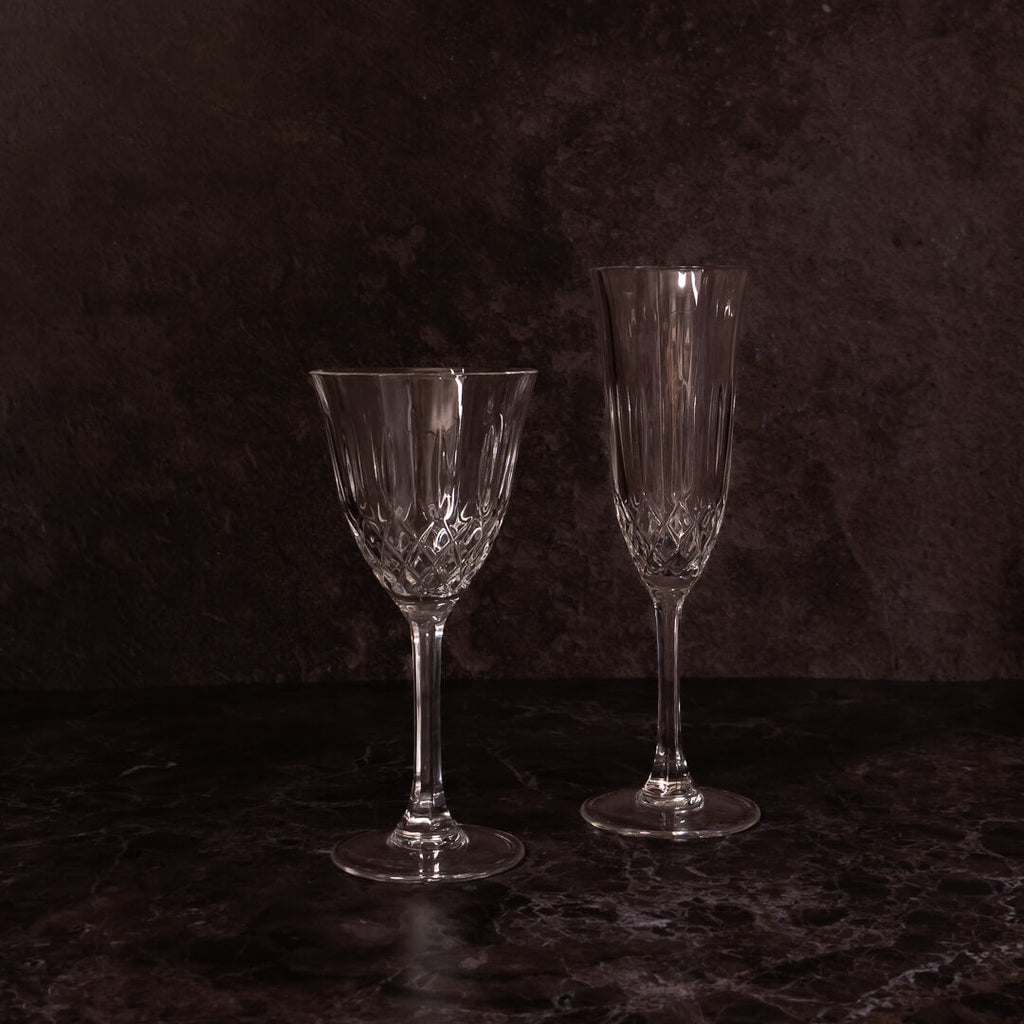 Vuokrattavat kristalliviini- ja kuohuviinilasit vierekkäin tummalla taustalla. Saman sarjan kirkkaat viinilasit häihin, juhliin ja eleganttiin kattaukseen.